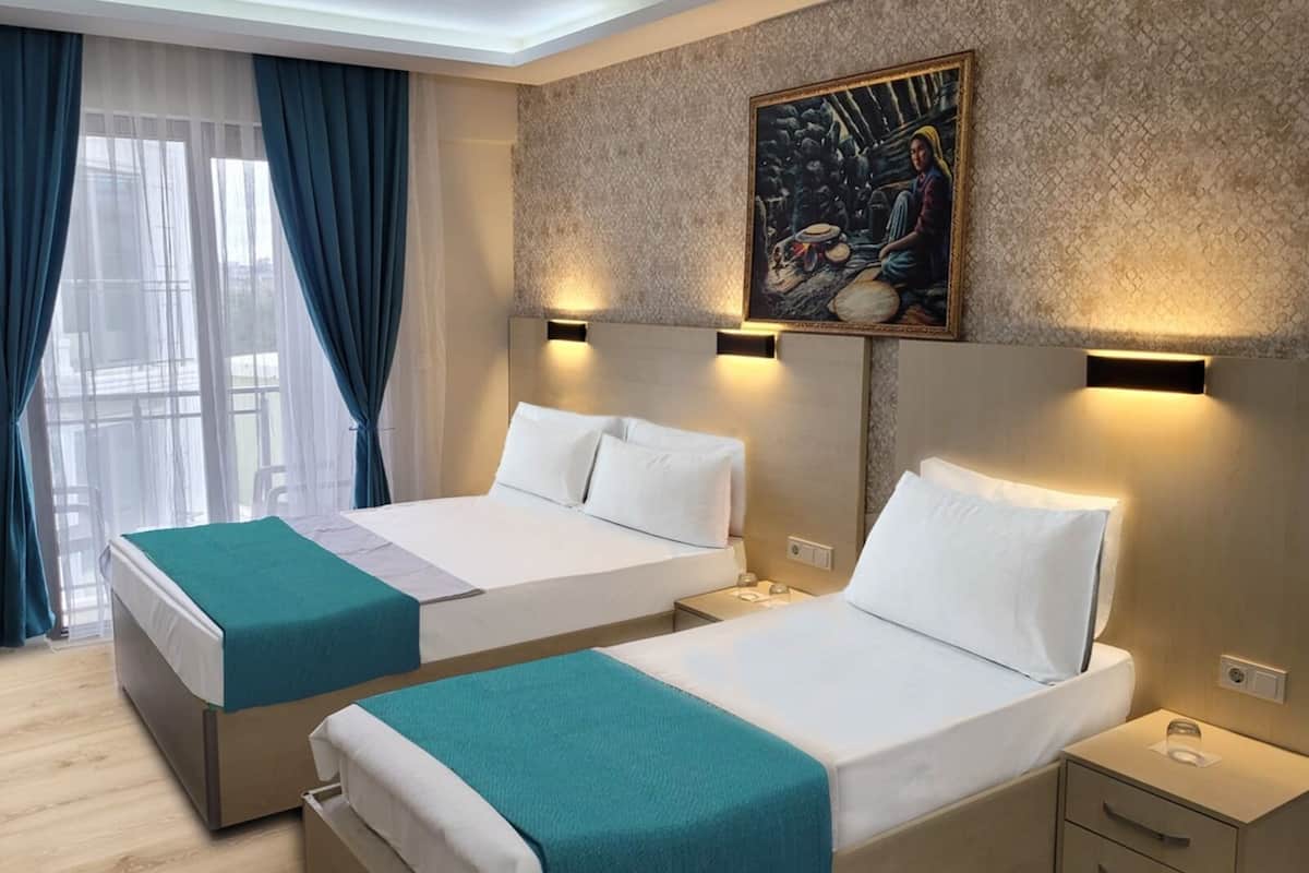 Habitación de hotel con dos camas, un ventanal con cortinas, un cuadro en la pared y una mesita de noche con lámpara.