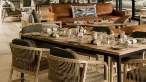 A spacious living area with a high ceiling, large windows, and a dining table set for four. - Zambezi Sands By Batoka (Victoria Falls)