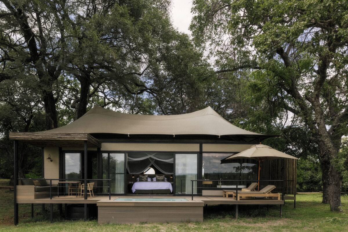 Alojamiento moderno al aire libre con un gran toldo, piscina y zona de terraza.