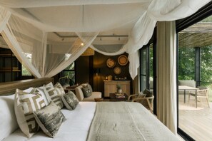 A bedroom with a large bed, a canopy, a desk, and a view of the outdoors. - Zambezi Sands By Batoka (Victoria Falls)