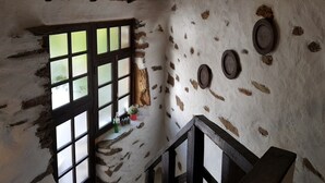 Een rustiek interieur met een houten plafond, een raam met ruitverdeling en een trap met houten leuning.