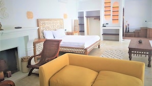 Ein Hotelzimmer mit Bett, Sofa, Schreibtisch, Kamin und Blick auf den Sonnenuntergang durch ein Fenster.