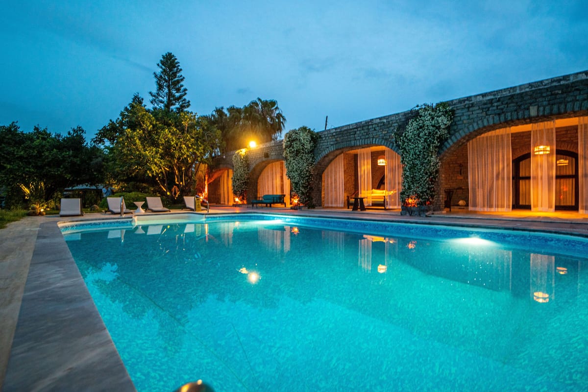 A swimming pool with lounge chairs and a stone building with arched windows.