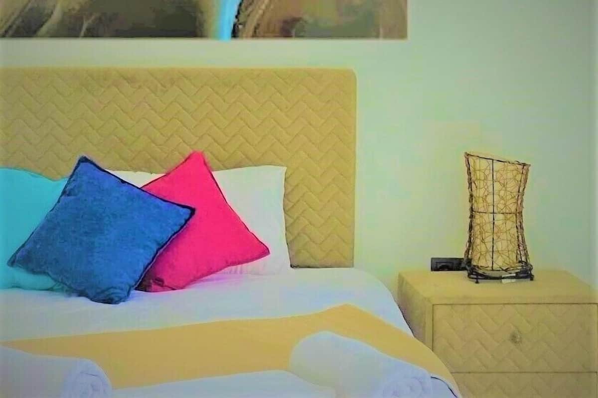 A bed with a quilted headboard, two pillows, and a bedside table with a decorative item.