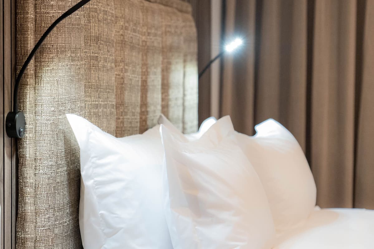 Un lit bien fait, avec du linge de lit blanc, une tête de lit à motifs et une table de chevet avec une lampe.