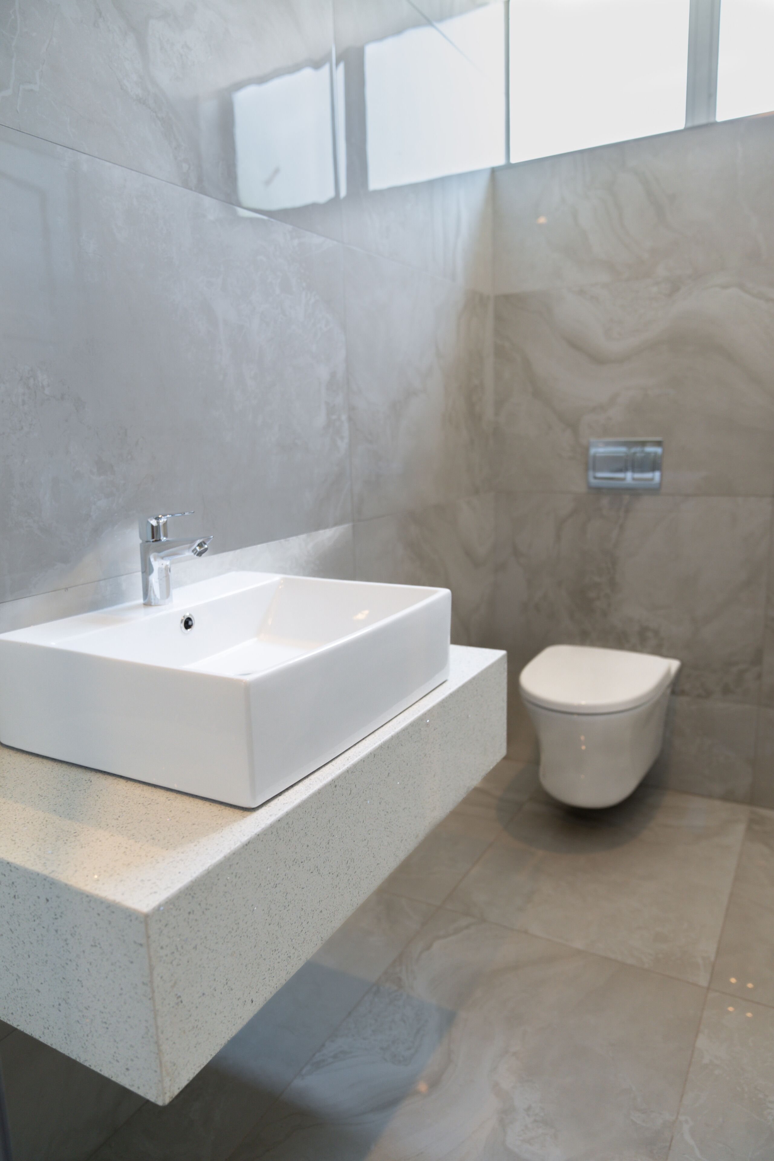 A modern bathroom with a rectangular sink, a toilet, and a marble wall.
