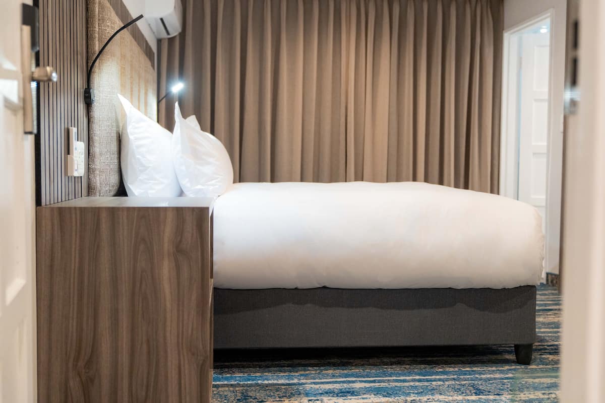 Un lit bien fait, avec une literie blanche, une table de chevet en bois et une lampe fixée au mur.