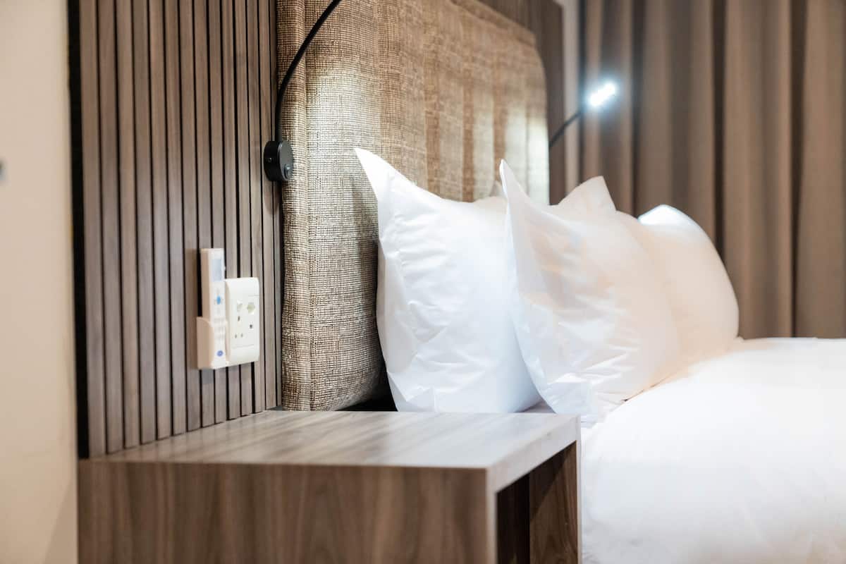 Un lit bien fait, avec des oreillers blancs et une tête de lit ornée de lignes verticales.