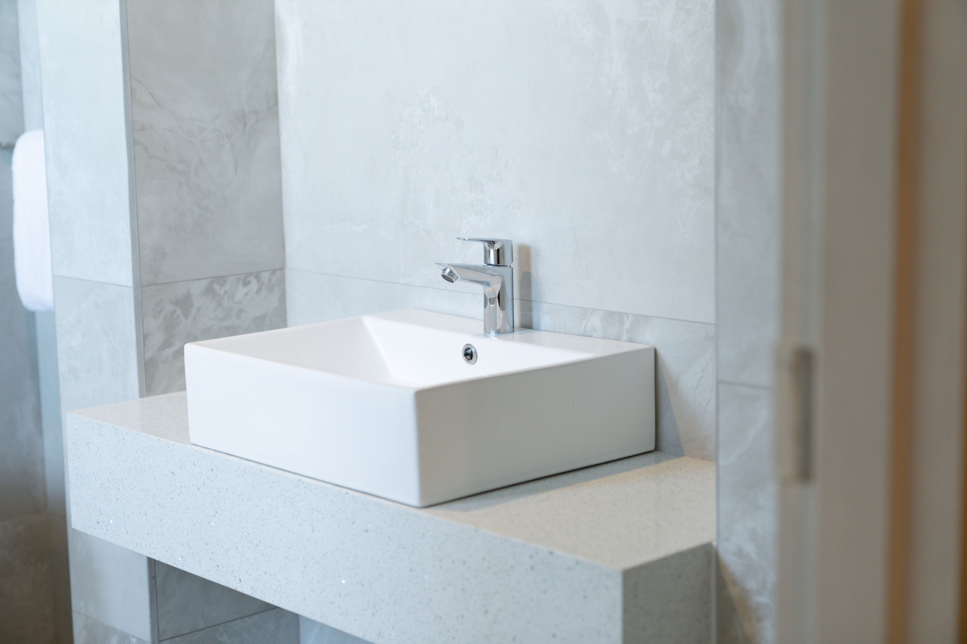 A modern bathroom with a rectangular white sink, chrome faucet, and a speckled countertop.