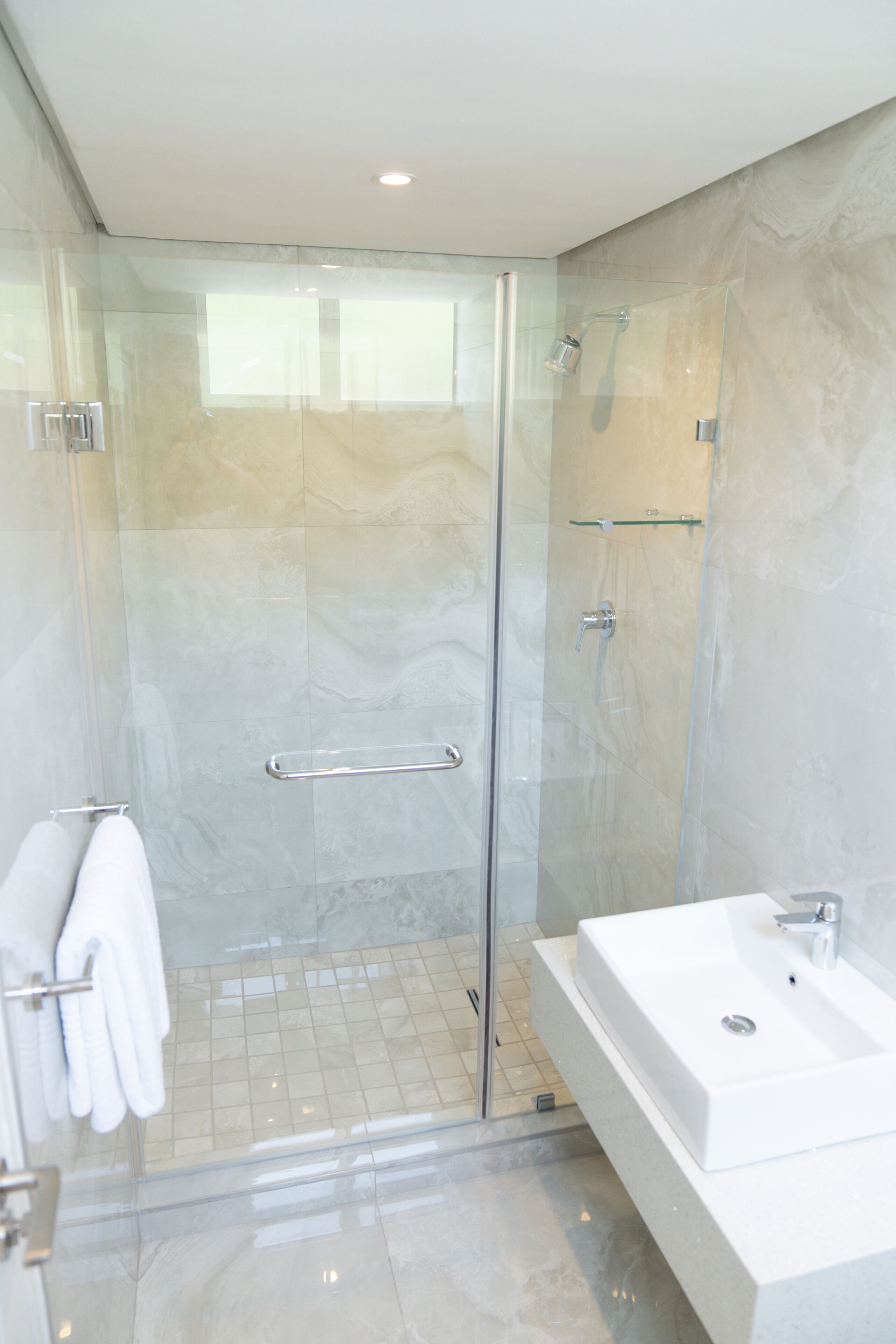 A modern bathroom with a glass-enclosed shower, a white sink, and a towel rack.