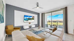 Ein modernes Wohnzimmer mit Wand-Fernseher, einer Couch, einem Couchtisch und einem Deckenventilator.