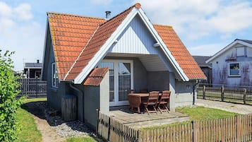 A small house with a tiled roof, a wooden deck, and a fenced yard.
