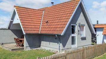 A modern house with a sloped roof, a small porch with chairs, and a wooden fence.