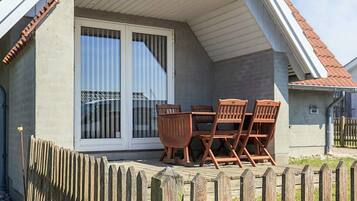 A covered patio area with a table and chairs, a wooden fence, and a house with a red-tiled roof.