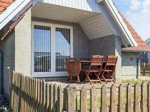 A covered patio area with a table and chairs, a wooden fence, and a house with a red-tiled roof. - 4 Person Holiday Home in Karrebaeksminde (Karrebæksminde)