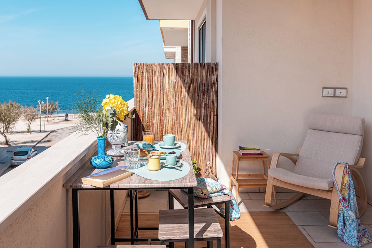 Een balkon met een eettafel, een stoel en uitzicht op zee.