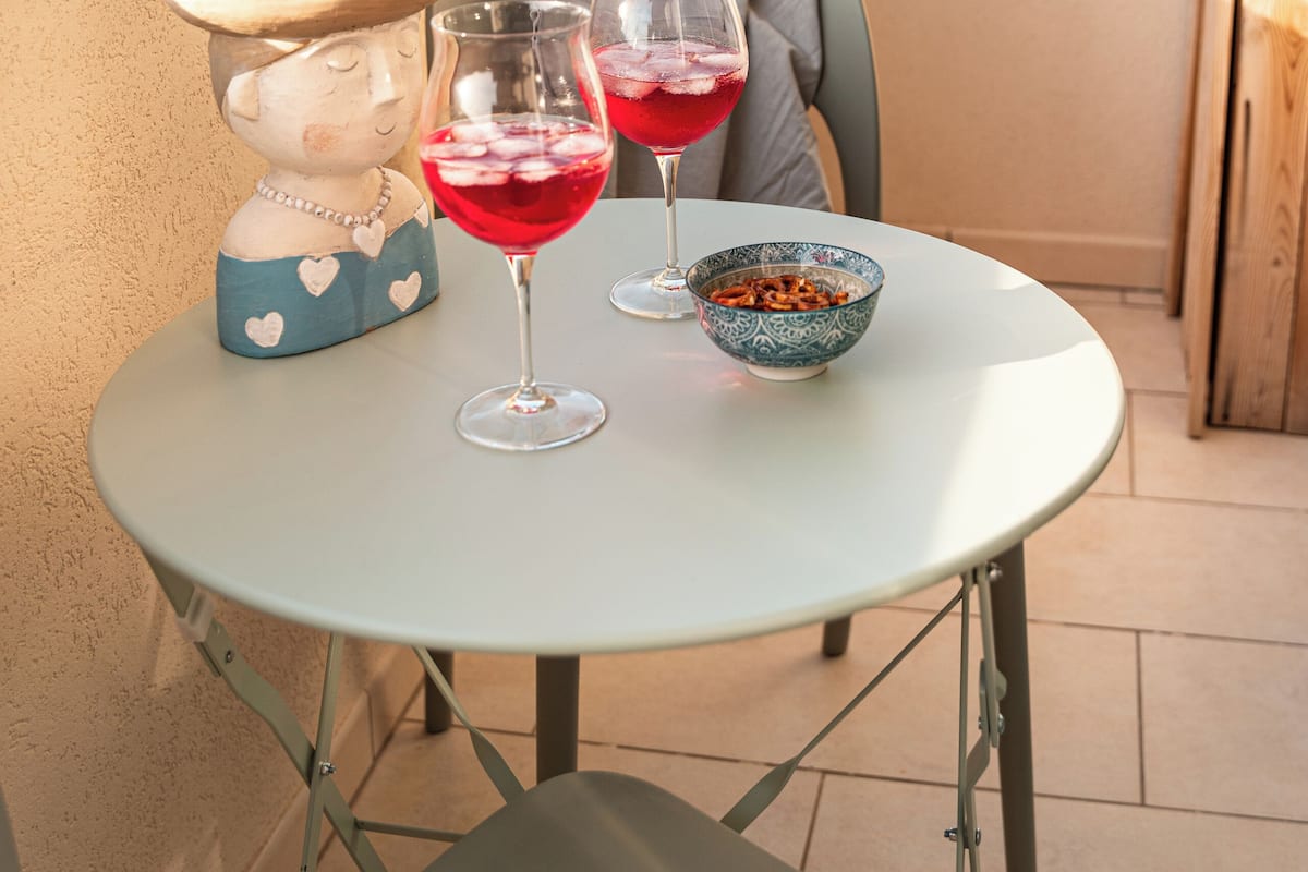 Een balkon met een tafel, twee glazen rode drank, een decoratief beeldje en een schaal.