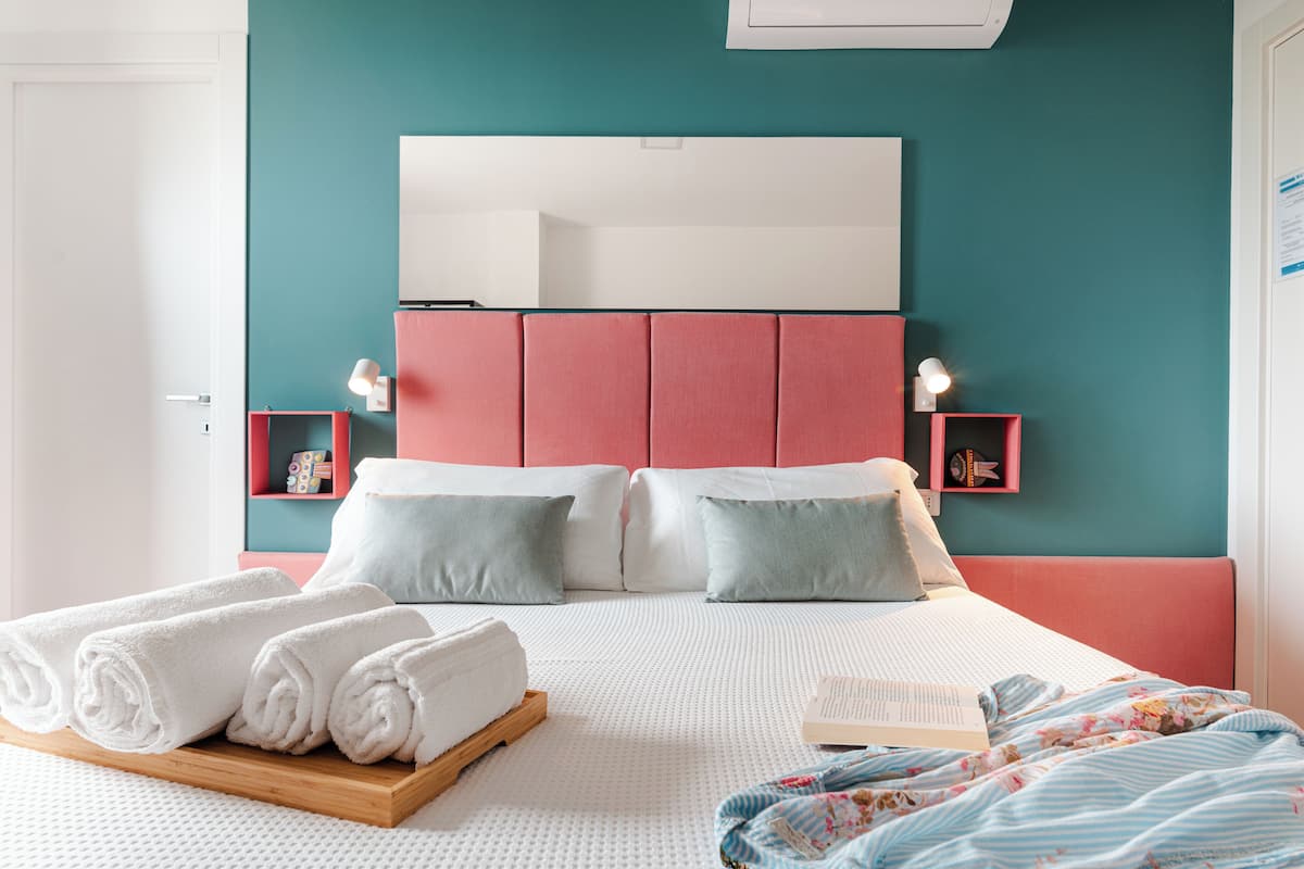 Een net opgemaakt bed met witte lakens, een houten dienblad met opgerolde handdoeken en een boek op het bed.