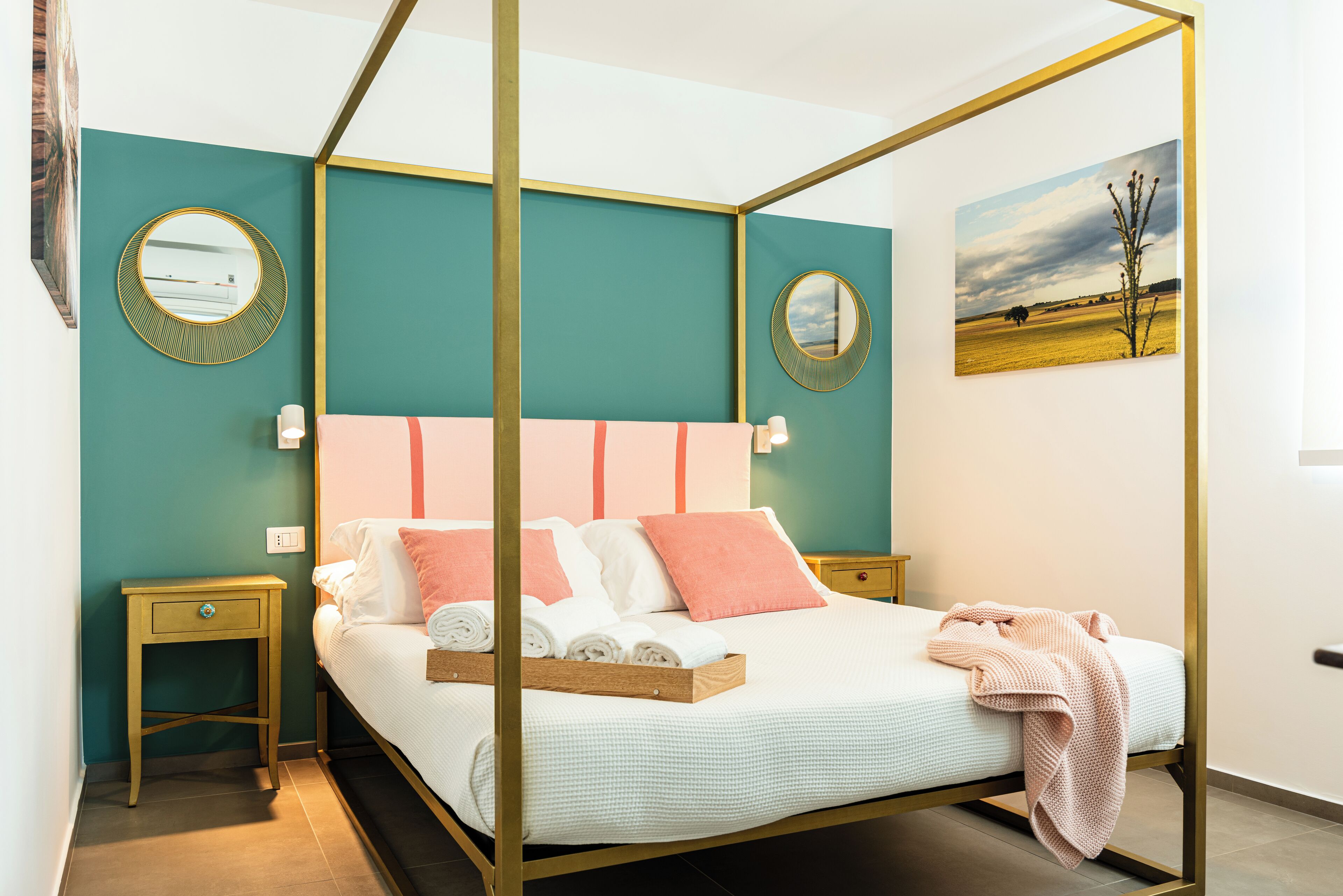 A four-poster bed with a teal wall and a landscape painting.