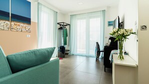 Una sala de estar moderna con un sofá azul turquesa, una zona de comedor con una silla negra, una mesita y un jarrón con flores.