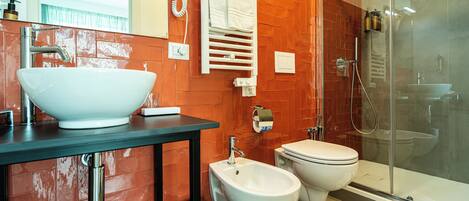 A modern bathroom with a large white sink, bidet, toilet, and glass-enclosed shower.