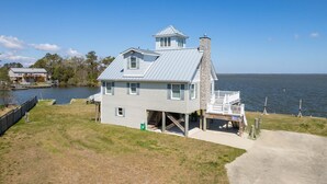 A waterfront house with a stone chimney, a covered porch, and a view of the lake. - Ohana 3 Bedroom Home in Walnut Island (Grandy)