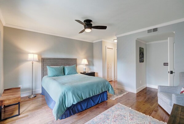 Une chambre à coucher avec un lit, des lampes de chevet, un ventilateur de plafond, une table de chevet et une porte.