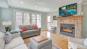 A spacious living room with a fireplace, a television mounted above it, and a large window with a view of a pool. - Echota Woods 221-Entry Level Condo, Gated Resort, Indoor/Outdoor Pools & Hot Tub (Boone)