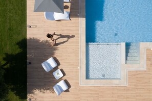 Vue aérienne d’un espace piscine avec une terrasse en bois, des chaises longues et une personne qui se promène.