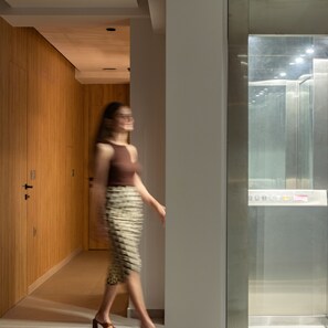 Un intérieur moderne avec des lambris en bois, un ascenseur en verre et un couloir.