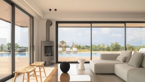 Una sala moderna con un gran ventanal que da a una piscina, un sofá, dos sillones de mimbre y una mesa de centro.