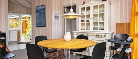 A dining area with a round table, black chairs, a white vase, and a cabinet with glassware.