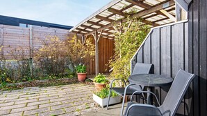 Une terrasse dotée d’une pergola en bois, de deux chaises en métal et de plantes en pot.