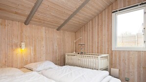 Une chambre avec deux lits, un berceau, une veilleuse et une fenêtre.