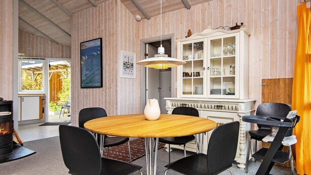 Un coin repas avec une table ronde, des chaises noires, un vase blanc et un meuble contenant de la verrerie.