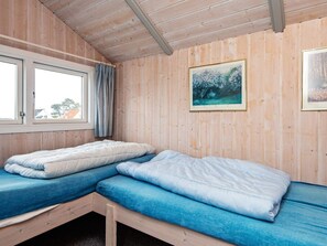 A room with two beds, wooden walls, a window with curtains, and a framed painting.