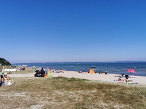 Uma praia com pessoas tomando sol e nadando, tendas e guarda-sóis.