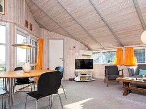 Quarto com teto de madeira, televisão, mesa com cadeiras e um sofá.