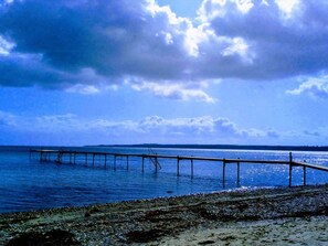 Un muelle se adentra en aguas tranquilas con una costa lejana bajo un cielo nublado.