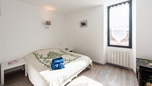 A bedroom with a bed, a bedside table, a lamp, a window, and a radiator. - Quiet and comfortable cottage (La Palme)