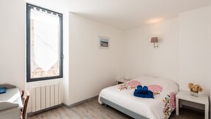 A bedroom with a bed, a bedside table, a nightstand, a window, and a wall-mounted lamp. - Quiet and comfortable cottage (La Palme)