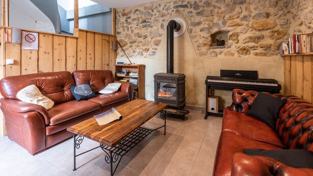 A cozy living room with a stone wall, a fireplace, a piano, and leather sofas. - Quiet and comfortable cottage (La Palme)