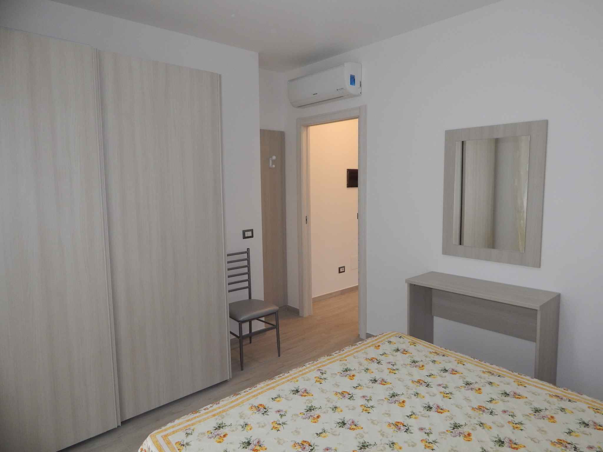 A bedroom with a bed, a desk, a chair, a wardrobe, and a mirror.