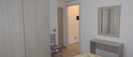 A bedroom with a bed, a desk, a chair, a wardrobe, and a mirror.