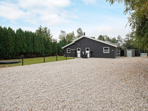 A black building with a gravel driveway, a fenced yard, and a wooded area in the background.