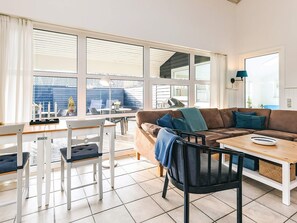 Una sala moderna con un sofá, sillas, una mesa de comedor y ventanas grandes.