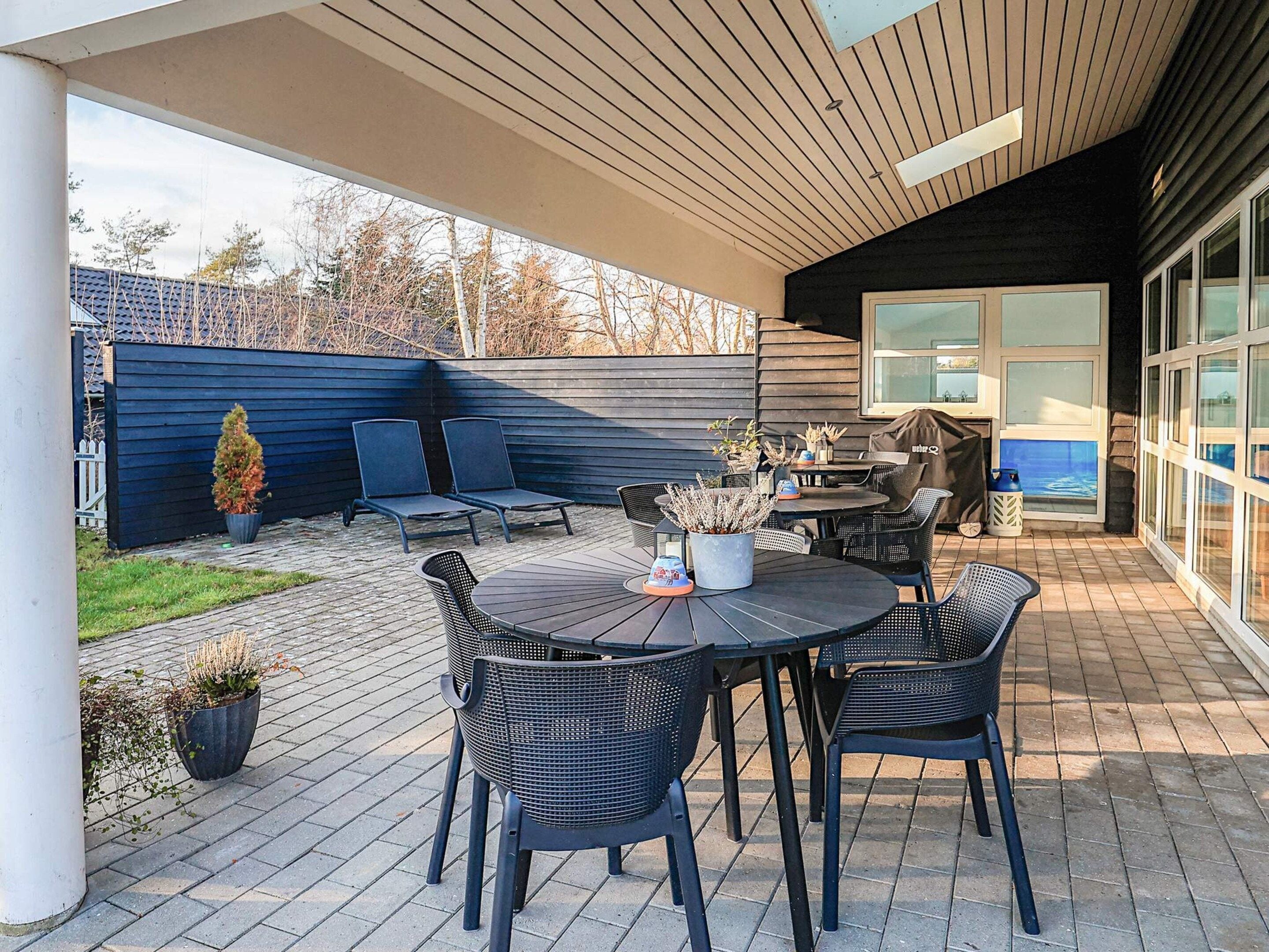 An outdoor patio with a round table and chairs, a small potted plant, and a covered seating area.