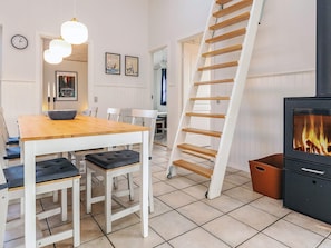 A modern living room with a wooden dining table, white chairs, a black sofa, a white staircase, and a black fireplace.