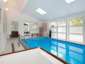 Una piscina interior con vistas al exterior, un banco de madera y una escalera.