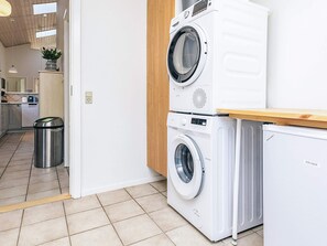 A laundry area with stacked washing machines and a compact dryer. - 4 Star Holiday Home in Vaeggerlose (Vaeggerlose)